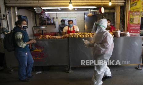 Seorang petugas mengenakan alat pelindung diri membawa sebotol alcohol untuk mensterilkan tangan pengunjung di pasar makanan grosir Central de Abasto, Mexico, Jumat (26/6). Sebagai negara pandemi dari Meksiko ke Argentina, petugas kesehatan berjuang untuk menahan wabah COVID-19 di pasar makanan tertutup yang menjadi ikon Amerika Latin.(AP Photo/Marco Ugarte)