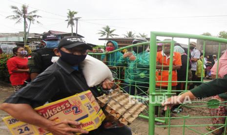 Seorang warga membawa paket sembako bansos yang diserahkan petugas kelurahan   (ilustrasi)