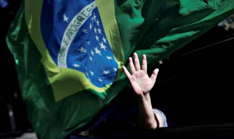 Seseorang melambai keluar dari jendela mobil saat pendukung Presiden Brazil Jair Bolsonaro melakukan protes atas tindakan karantina, di tengah penyebaran penyakit virus korona (COVID-19) di Sao Paulo, Brazil, Minggu (17/5/2020). (Reuters/Amanda Perobelli)