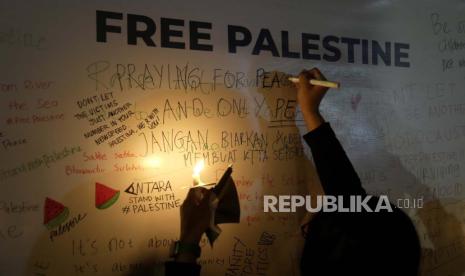 Seorang aktivis menulis di dinding pesan saat menyalakan lilin untuk mendukung Palestina di Kedutaan Besar Palestina di Jakarta, Indonesia, Kamis, 2 November 2023.