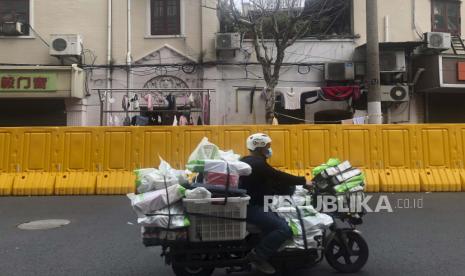 Seorang pengantar barang melewati penghalang yang dipasang untuk mengunci sebuah komunitas di Shanghai, Cina, Rabu, 30 Maret 2022. Shanghai memperpanjang kebijakan lockdown atau karantina wilayah di timur dan barat wilayahnya, Kamis (31/3) waktu setempat. 