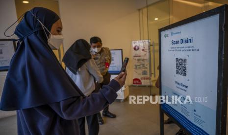 Pengunjung memindai kode batang aplikasi PeduliLindungi di pintu masuk sebuah pusat perbelanjaan.