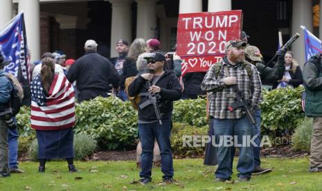 Dalam foto file 6 Januari 2021 ini, dua pria berdiri bersenjata di depan Rumah Gubernur di Olympia, Washington, selama protes mendukung Presiden Donald Trump dan menentang penghitungan suara elektoral di Washington, DC, menegaskan Kemenangan Presiden terpilih Joe Biden. Setelah siklus pemilu 2020 yang didominasi oleh teori konspirasi dan klaim palsu tentang pemungutan suara, pejabat tinggi pemilu di seluruh negeri menanti pemilu di masa depan dan bergulat dengan bagaimana mereka dapat melawan gelombang informasi yang salah yang menyebabkan ancaman kekerasan terhadap mereka dan akhirnya kerusuhan yang mematikan. di Capitol.