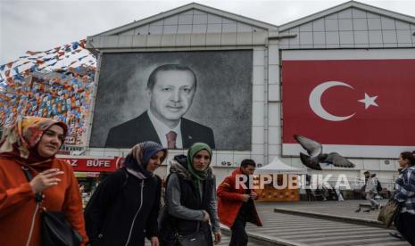 Orang-orang melewati potret Presiden Turki Recep Tayyip Erdogan dan bendera Turki di Bursa, Turki, Kamis (11/5/2023). Turki akan mengadakan pemilihan umum pada 14 Mei 2023 dengan sistem dua putaran untuk memilih presidennya, sedangkan pemilihan parlemen akan diadakan secara serentak .