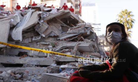  Seorang penduduk setempat, yang tinggal di luar ruangan karena takut akan gempa susulan, menyaksikan anggota layanan penyelamatan mencari korban di puing-puing bangunan yang runtuh di Izmir, Turki, Sabtu, 31 Oktober 2020. Tim penyelamat pada hari Sabtu menerobos blok beton dan puing-puing dari delapan bangunan runtuh di kota terbesar ketiga Turki untuk mencari korban gempa bumi dahsyat yang melanda pantai Aegean Turki dan utara pulau Samos Yunani, menewaskan puluhan Ratusan lainnya terluka.