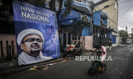 Anak-anak menaiki skuter di depan spanduk Imam Besar Front Pembela Islam (FPI) Habib Rizieq Shihab yang terpasang di kawasan Petamburan III, Jakarta, Rabu (30/12). Pemerintah resmi membubarkan dan menghentikan segala aktivitas FPI sebagai organisasi masyarakat maupun organisasi pada umumnya. Republika/Putra M. Akbar