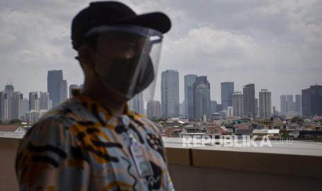 Warga mengenakan masker dan pelindung wajah saat beraktivitas dengan latar belakang gedung bertingkat di kawasan Pejompongan, Jakarta. Satgas meminta daerah yang kasus kenaikan Covid-19 tinggi untuk fokus menekan penyebaran virus corona. Riau, Jawa Timur, dan DKI Jakarta masuk daerah prioritas karena tren laju kasusnya tinggi.