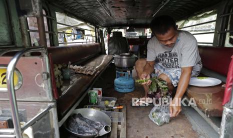 Pengemudi  jeepney Michael Navarra memasak ikan dan sayuran di atas kompor portabel mereka di dalam jeepney di terminal Tandang Sora yang telah menjadi rumah mereka sejak lockdown dimulai tiga bulan lalu di kota Quezon, Filipina, Rabu (17/6). Sekitar 35 pengemudi jeepney terpaksa tetap tinggal di terminal akibat adanya pembatasan perjalanan dan menjadikan jeepney sebagai tempat tinggal karena pemerintah melarang angkutan umum beroprasi selama masyarakat isolasi diri untuk mencegah penyebaran Covid-19. Banyak pengemudi yang menganggur dan terpaksa mengemis di jalan-jalan, memajang papan nama bertuliskan permohonan uang dan makanan di jipney mereka. Foto AP / Aaron Favila 