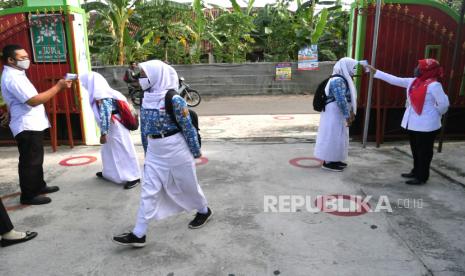 Guru mengecek suhu tubuh siswa sebelum pembelajaran tatap muka di SMPN 1 Gantiwarno, Klaten, Jawa Tengah, Rabu (14/10). Dinas Pendidikan Klaten menunjuk lima sekolah menengah pertama untuk ujicoba pembelajaran tatap muka. Setiap kelas hanya berisi 10 siswa dan menggunakan protokol kesehatan Covid-19 ketat. Sesi tatap muka berlangsung selama satu jam. Pada pekan pertama diberikan materi tentang Covid-19, pekan kedua materi pembelajaran teknologi informasi. Dan memasuki mata pelajaran pada pekan ketiga. Pembelajaran dimulai pukul 07.00 hingga 08.00 untuk kelas 7, pukul 08.00 hingga 09.00 untuk kelas 8, dan 09.00 hingga 10.00 kelas 10.