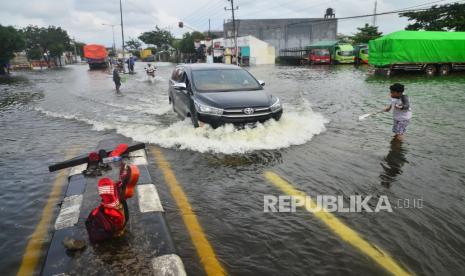 Warga mengatur lalu lintas di jalan jalur Pantura yang tergenang banjir, Desa Jati Wetan, Kudus, Jawa Tengah, Ahad (7/2/2021). Banjir dengan ketinggian hingga 50cm akibat curah hujan tinggi itu menyebabkan kemacetan dari arah Kudus menuju Semarang sejak Sabtu (6/2) lalu. 