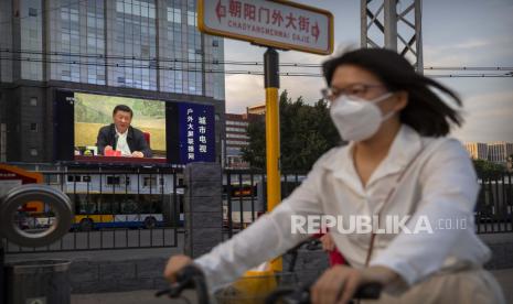 Seorang wanita mengenakan masker untuk melindungi terhadap virus corona baru naik sepeda melewati layar video besar yang menunjukkan Presiden Cina Xi Jinping berbicara di Beijing, Selasa, 30 Juni 2020. China menyetujui undang-undang keamanan nasional yang kontroversial yang akan memungkinkan pihak berwenang untuk menindak tentang kegiatan subversif dan pemisahan diri di Hong Kong, sebuah langkah yang dianggap banyak orang sebagai yang paling berani di Beijing untuk menghapus firewall hukum antara wilayah semi-otonom dan sistem Partai Komunis otoriter daratan. 