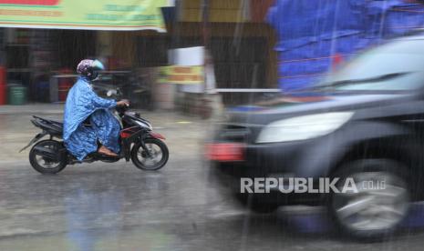 Pengendara menerobos hujan di jalan. 