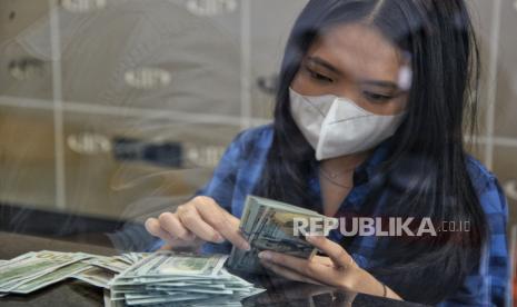 Petugas menghitung uang dolar AS di gerai penukaran mata uang asing.