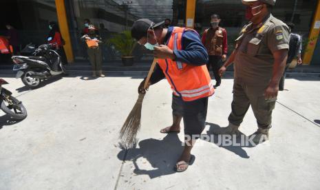 Warga yang melanggar protokol kesehatan COVID-19 menyapu bahu jalan saat terjaring dalam Operasi Yustisi  di Palu, Sulawesi Tengah, Kamis (10/1/2020). Pemerintah Kota Palu mulai memberikan sanksi kepada warga yang melanggar protokol kesehatan COVID-19. Selain melakukan penindakan dan pemberian sanksi, Pemerintah Kota Palu juga memperketat perbatasan wilayah dengan mewajibkan rapid test bagi pelaku perjalanan yang akan masuk ke wilayah Kota Palu guna mencegah penyebaran COVID-19 yang terus meningkat.