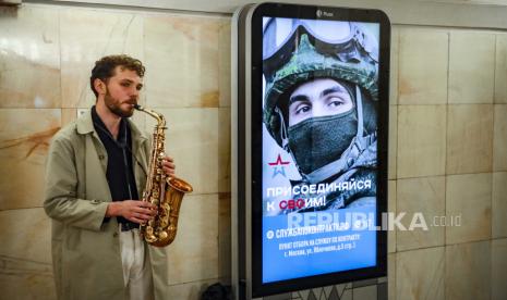 Seorang pengamen memainkan saksofon dengan poster yang mengiklankan wajib militer yang menunjukkan seorang tentara Rusia dan slogan Bergabunglah dengan Anda di sebuah stasiun metro di Moskow, Rusia, 03 Mei 2023.  Kelompok tentara bayaran Rusia, Wagner, pada hari Ahad (7/5/2023) membatalkan rencana mereka untuk mundur dari Bakhmut di Ukraina timur.