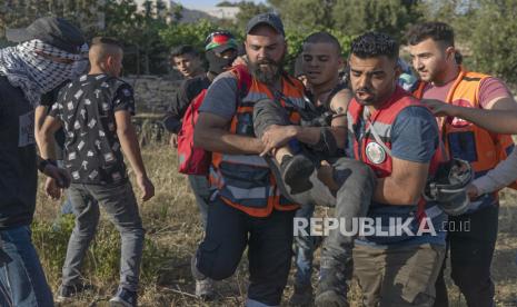 Paramedis mengevakuasi pengunjuk rasa Palestina yang terluka selama bentrokan dengan tentara Israel di pintu masuk utara kota Ramallah, Tepi Barat, Minggu, 16 Mei 2021.