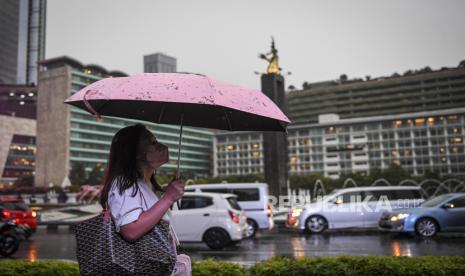 Seorang warga menggunakan payung saat turun di kawasan Bundaran Hotel Indonesia, Jakarta.