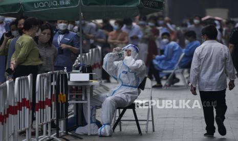 Seorang pekerja dengan alat pelindung minum air saat warga mengantre untuk tes COVID-19 di luar lingkungan di Beijing.