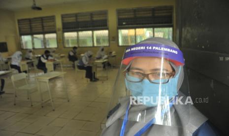 Guru mengenakan Alat Pelindung Diri saat mengawasi para calon siswa yang mengikuti tes tertulis sebagai bagian dari proses Penerimaan Peserta Didik Baru (PPDB) di SMA Negeri 14 Palembang, Sumsel, Rabu (24/6/2020). Dinas Pendidikan Kota Palembang menerapkan protokol kesehatan pada tes tertulis  PPDB yang diselenggarakan serentak se-Kota Palembang. Provinsi Sumatra Selatan tidak memiliki zona merah COVID-19 atau wilayah risiko tinggi berdasarkan peta terbaru dari Gugus Tugas Percepatan Penanganan COVID-19 pusat per 12 Juli 2020, meski kasus baru terus bertambah.