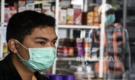 Pegawai apotek mengenakan masker melayani pembeli di balik sekat di Apotek Contong, Jalan Warung Contong, Kota Cimahi, Ahad (5/4). Presiden Joko Widodo mengimbau seluruh warga saat ini wajib mengenakan masker saat berada di luar rumah. Hal itu dilakukan guna menghindari penularan virus corona baru penyebab Covid-19.