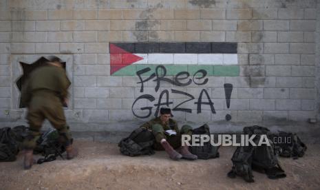 Seorang tentara Israel membaca dari sebuah buku di sebelah grafiti yang menampilkan bendera Palestina, selama latihan perang kota di fasilitas pelatihan tentara di pangkalan militer Zeelim, Israel selatan, 9 November 2021. Sejak awal tahun, Israel dilaporkan mulai melakukan langkah untuk menyensor kurikulum sekolah-sekolah yang ada di Yerusalem bagian timur, salah satunya dengan menghapus foto-foto masjid Al Aqsa. 