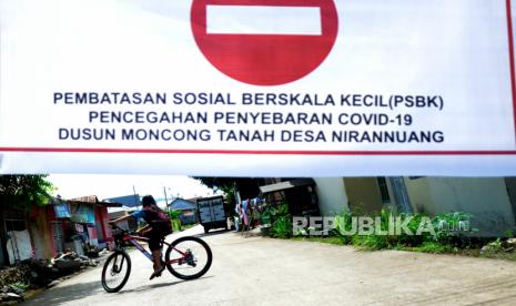 Seorang anak bermain sepeda di dekat pengumuman pembatasan sosial pada akses masuk pedesaan di Desa Romangloe, Kabupaten Gowa, Sulawesi Selatan, Kamis (16/4/2020). Sejumlah pedesaan di Kabupaten Gowa  memberlakukan karantina wilayah secara mandiri dengan menutup akses masuk perkampungan bagi warga luar dan pemudk untuk memutus penyebaran COVID-19