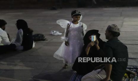 Seorang gadis Muslim India berpakaian peri bermain dengan keluarganya setelah berbuka puasa pada hari pertama bulan suci Ramadhan di Masjid Jama di New Delhi, India, Ahad, 3 April 2021.