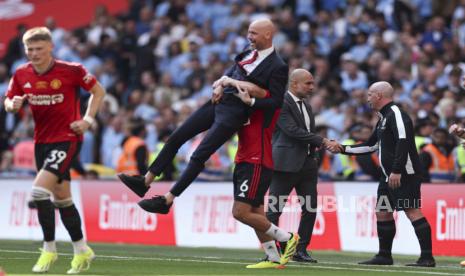 Pelatih kepala Manchester City Pep Guardiola berjabat tangan dengan seorang ofisial saat Lisandro Martinez dari Manchester United mengangkat pelatih kepala Manchester United Erik ten Hag saat merayakan kemenangan dalam pertandingan sepak bola final Piala FA Inggris antara Manchester City dan Manchester United di Stadion Wembley di London, Sabtu, (25/5/2024).