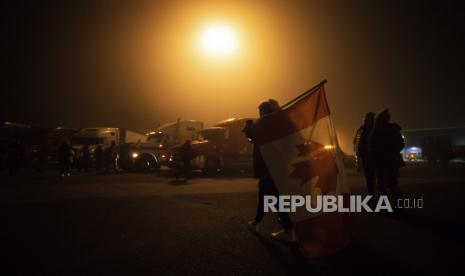 Seorang wanita membawa bendera Kanada terbalik di bahunya sebelum konvoi pengemudi truk dan pendukung lintas negara berangkat ke Ottawa untuk memprotes mandat vaksin federal untuk pengemudi truk di Delta, B.C. pada hari Ahad, 23 Januari 2022. 