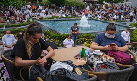 Para wanita menikmati waktu mereka di sebuah kafe sementara orang-orang menghadiri sholat Jumat dengan jarak sosial di kolam Eminonu Square, di tengah pandemi penyakit COVID-19 yang disebabkan oleh coronavirus SARS-CoV-2 di Istanbul, Turki, 26 Juni 2020. Pihak berwenang Turki sekarang telah memungkinkan pembukaan kembali restoran, kafe, taman dan pantai, serta mencabut larangan perjalanan antar kota, karena negara itu memudahkan pembatasan yang telah diberlakukan dalam upaya untuk membendung penyebaran pandemi berkelanjutan COVID- 19 penyakit yang disebabkan oleh coronavirus SARS-CoV-2.