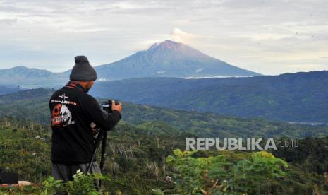 Fotografer bersiap memotret Gunung Kerinci yang sedang mengembuskan gas dan material ke udara yang terlihat dari Desa Belui, Depati Tujuh, Kerinci, Jambi, Jumat (4/11/2022). Gunung dengan ketinggian 3.805 mdpl yang masih berada pada level II (waspada) itu kembali mengalami gempa embusan yang terpantau secara visual pada Jumat pagi. 