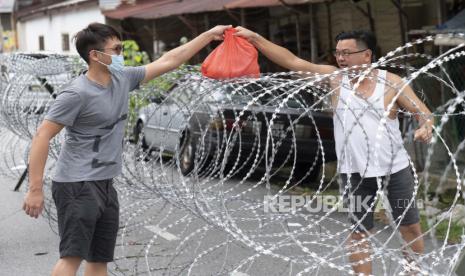 Seorang lelaki memberikan persediaan makanan melalui kawat berduri di area lockdown Selayang Baru, di luar Kuala Lumpur, Malaysia, Ahad (26/4). Lockdown tersebut dilakukan untuk memungkinkan aparat berwenang dalam melakukan penyaringan dan membantu mencegah penyebaran coronavirus