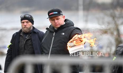 Pemimpin partai politik sayap kanan Denmark Stram Kurs, Rasmus Paludan, membakar sebuah mushaf Alquran, sambil diawasi oleh petugas polisi, saat dia melakukan protes di luar Kedutaan Besar Turki di Stockholm, Swedia, 21 Januari 2023.