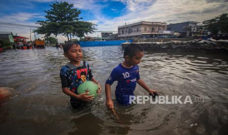 Dua bocah bermain di kawasan yang terendam banjir di Total Persada, Kota Tangerang, Banten, Ahad (22/3). 