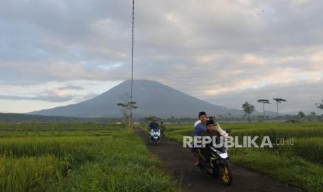 Warga menaiki sepeda motor dengan latar belakang Gunung Semeru mengeluarkan asap yang tampak dari Desa Supiturang, Pronojiwo, Lumajang, Jawa Timur. ilustrasi