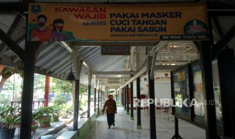 Seorang guru melintas samping aula di SMPN 10 Kota Tegal, Jawa Tengah, Kamis (6/8/). Menurut pihak sekolah, SMPN 10 Kota Tegal menghentikan pembelajaran tatap muka hingga waktu yang belum ditentukan dan kembali pembelajaran secara daring, akibat orangtua salahsatu siswa positif Covid-19. (ilustrasi)