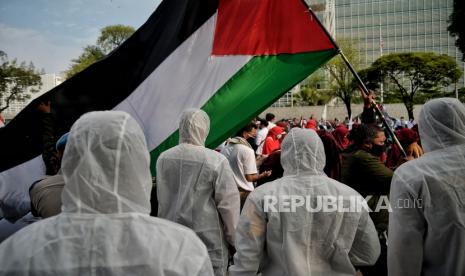 Petugas kepolisian menggunakan pakaian Alat Pelindung Diri (APD) membantu masa aksi untuk menerapkan protokol kesehatan saat aksi solidaritas bela Palestina di depan Gedung Kedubes Amerika Serikat, Jakarta, Selasa (18/5). Dalam aksi tersebut Polres Metro Jakarta Pusat mengamankan tiga orang warga negara asing (WNA).. Republika/Thoudy Badai