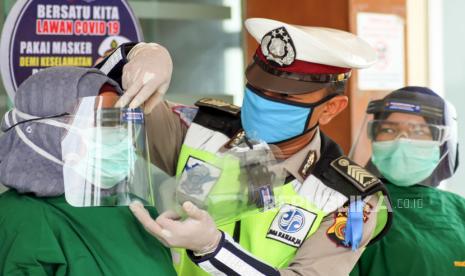 Personel polisi satuan lalu lintas membantu memakaikan pelindung wajah tenaga medis rumah sakit rujukan penanganan Covid-19.