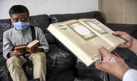 Akbar (kiri) didampingi Direktur LAZ Al-Hilal Iwan Setiawan (kanan) membaca Al-Quran di Kantor Pusat Pesantren Yatim Al-Hilal, Jalan Gegerkalong Hilir, Kota Bandung, Rabu (4/11). Muhammad Al-Gifari atau Akbar yang sehari-hari menjadi pemulung tersebut kini menjadi sosok yang viral dan menjadi perhatian masyarakat karena fotonya yang sedang membaca Al-Quran saat menunggu hujan reda di Jalan Braga, Kota Bandung. Foto: Abdan Syakura/Republika