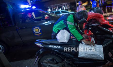 Pengendara ojek online mengemas pesanan saat patroli pengamanan pembatasan sosial berskala besar (PSBB) di kawasan Dr. Satrio, Jakarta Selatan, Jumat (10/4)