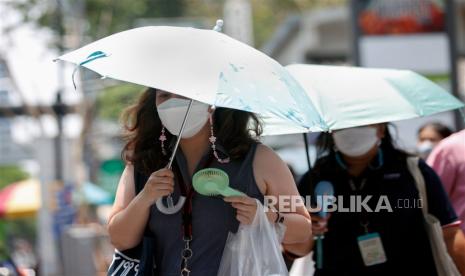  Pekerja kantoran menggunakan payung untuk melindungi sinar matahari dan mendinginkan diri dengan kipas genggam elektrik saat cuaca panas di Bangkok, Thailand, Jumat (28/4/2023). 