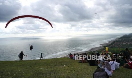 Wisatawan duduk pada landasan menonton terbang tandem dengan paralayang di Wisata Watu Gupit, Purwosari, Gunung Kidul, Yogyakarta.