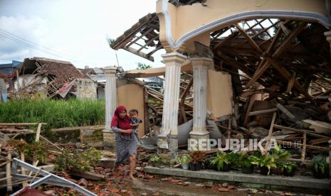 Pengungsi berjalan di depan bangunan yang roboh akibat gempa di Desa Gasol, Kecamatan Cugenang, Kabupaten Cianjur, Jawa Barat, Jumat (25/11/2022).