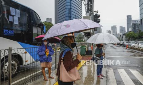 Orang-orang memegang payung di bawah hujan, melintasi jalan yang sibuk di Jakarta. Badan Meteorologi, Klimatologi, dan Geofisika (BMKG) Indonesia telah mengeluarkan peringatan publik untuk cuaca ekstrem (ilustrasi).