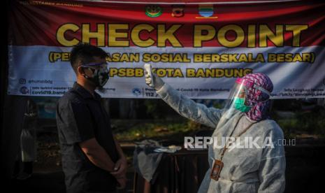 Petugas memeriksa suhu tubuh di titik pemeriksaan pelaksanaan Pembatasan Sosial Berskala Besar.