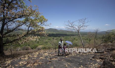 A Sri Lankan man climbs a rock in a forest reserve with a child to access the child