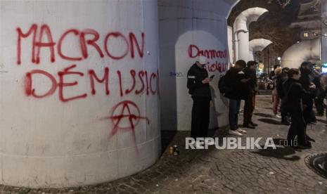 Demonstran berdiri di samping grafiti bertuliskan 