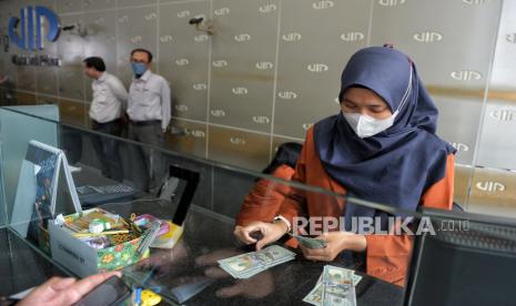 Petugas menghitung uang dolar AS di tempat penukaran valuta asing.