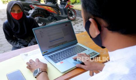 Seorang guru membantu wali murid mengisi data saat Penerimaan Peserta Didik Baru (PPDB) daring jalur zonasi tingkat SMP di SD Negeri Pesantren 2, Kota Kediri, Jawa Timur, Kamis (25/6/2020). Sejumlah SD di daerah itu membuka layanan bantuan pendaftaran PPDB daring ke jenjang SMP kepada alumninya agar tidak terjadi kesalahan dalam mendaftar karena kekurangtahuan wali murid. ANTARA FOTO/Prasetia Fauzani/nz