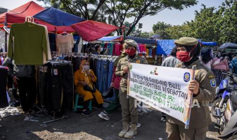 Petugas Satpol PP melakukan sosialisasi protokol kesehatan kepada warga saat kegiatan patroli senyum edukasi protokol kesehatan 5M di Pasar Tumpah di kawasan Monumen Perjuangan Rakyat Jawa Barat, Kota Bandung, Ahad (5/9). Patroli Senyum yang digelar oleh Satpol PP Provinsi Jawa Barat bersama Satpol PP Kota Bandung, Kelompok Penyanyi Jalanan dan Kelompok Pedagang Kaki Lima tersebut bertujuan untuk memberikan edukasi, kampanye serta mengajak masyarakat untuk selalu menerapkan protokol kesehatan pencegahan Covid-19. Foto: Republika/Abdan Syakura